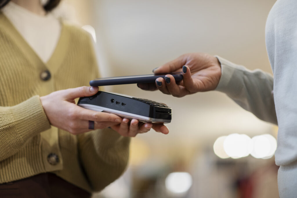 A person making a contactless payment with a smartphone on a card reader machine.
