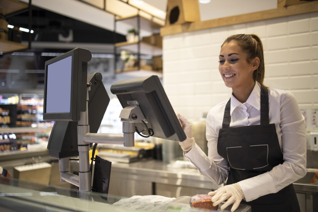 Woman in apron smiling while using touchscreen EPOS system at retail checkout counter
